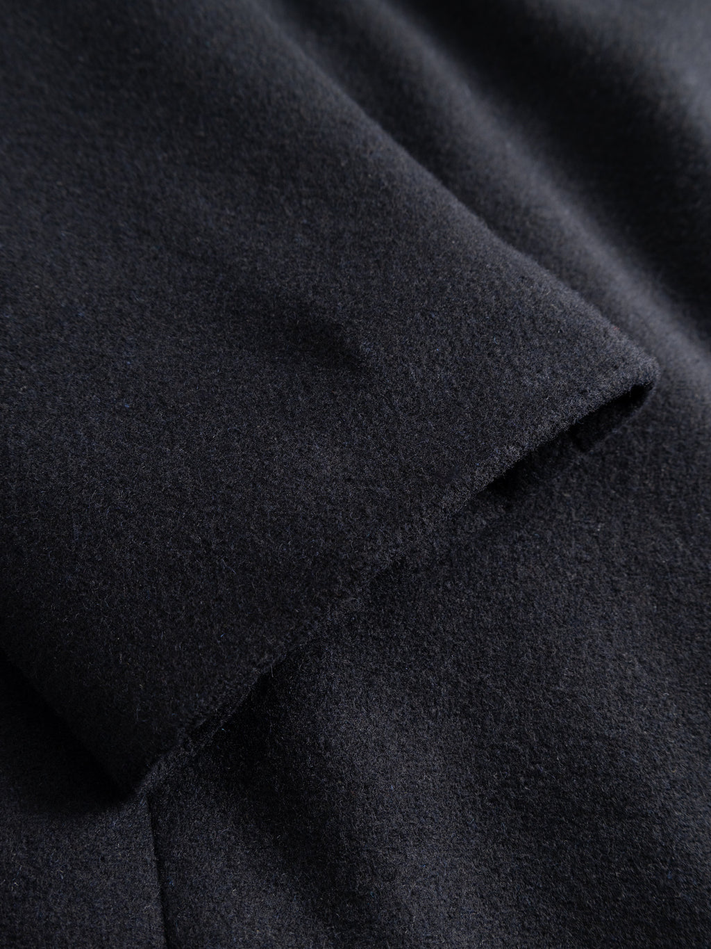 Close-up of the sleeve of the GABleeds Plain Coat in navy by Gabba, showcasing the fabric’s texture and precise stitching details. The image emphasizes the soft, slightly fuzzy surface and crisp edge of the sleeve, making this coat a timeless choice for outerwear and everyday style.
