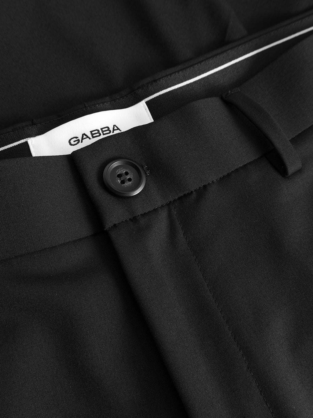 Close-up of the waistband of Gabba GABjoli Tailor Dressy Shorts in black, showing a black button, belt loop, and white GABBA label. These shorts feature a relaxed fit for extra comfort.