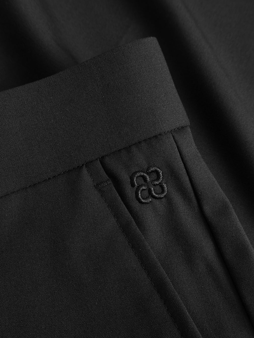 Close-up of Gabba GABjoli Tailor Dressy Shorts in black, featuring a smooth, matte waistband, pocket seam, and a small four-loop embroidered logo near the pocket for a refined look.