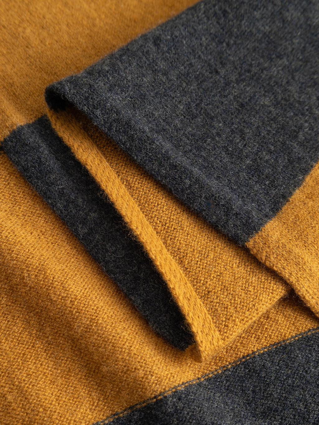 Close-up of the Gabba GABwest Aico Scarf - Yellow Stripes, featuring wide mustard yellow and dark gray stripes. The soft, textured surface and clean edges highlight this merino wool scarf as an ideal winter accessory.