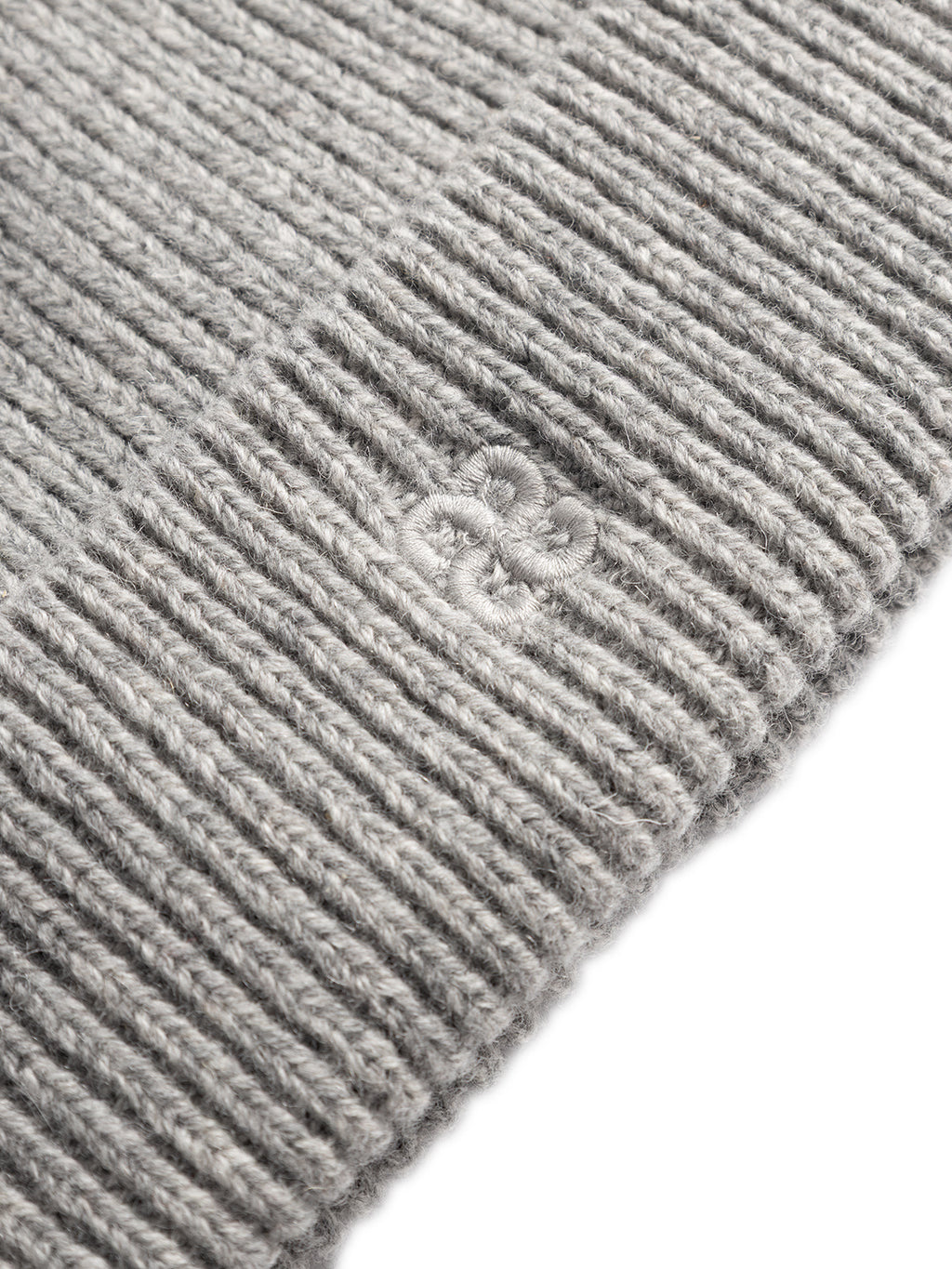 Close-up of the GABeast Flash Beanie - Grey Mel by Gabba, featuring a gray ribbed knit fabric that’s ideal for winter accessories. The beanie showcases an embroidered logo in matching gray thread on its folded edge, set against a white background.