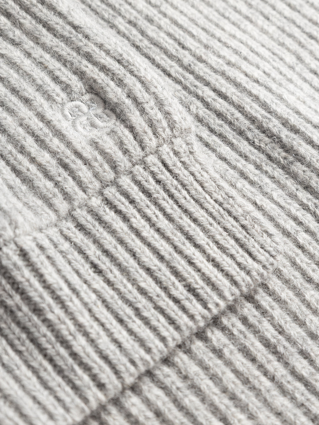 Close-up of the Gabba GABeast Flash Scarf in Grey Mel—a light gray rib-knit scarf featuring a folded section and a small embroidered “ae” logo, making it the perfect cozy winter accessory.