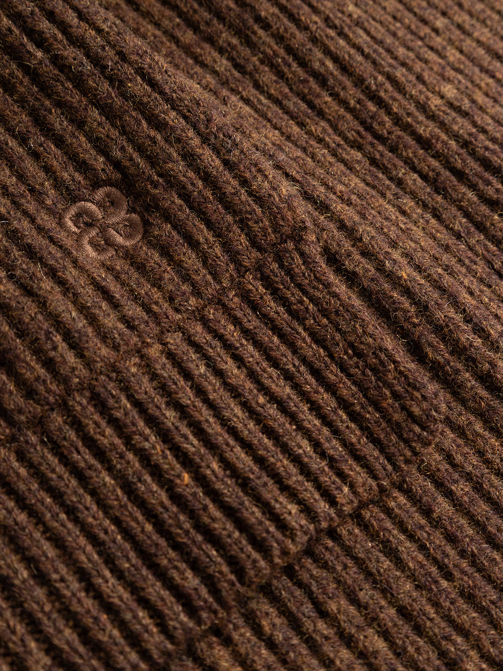 Close-up of the GABeast Flash Scarf - Brown Slate by Gabba, featuring brown ribbed knit fabric with a subtle embroidered logo on the left side. The wool texture and intricate stitches are clearly visible, showcasing the scarf’s softness and warmth—making it an ideal winter accessory.