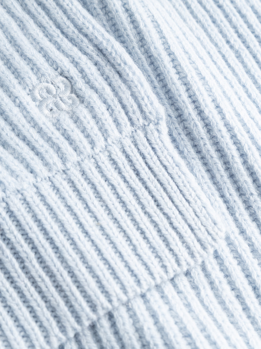 Close-up of the GABeast Flash Scarf by Gabba in Dusty Blue, featuring light blue ribbed fabric with a subtle embroidered flower detail that highlights its inviting texture and fine stitching—perfect for adding cozy style to your favorite winter accessory collection.