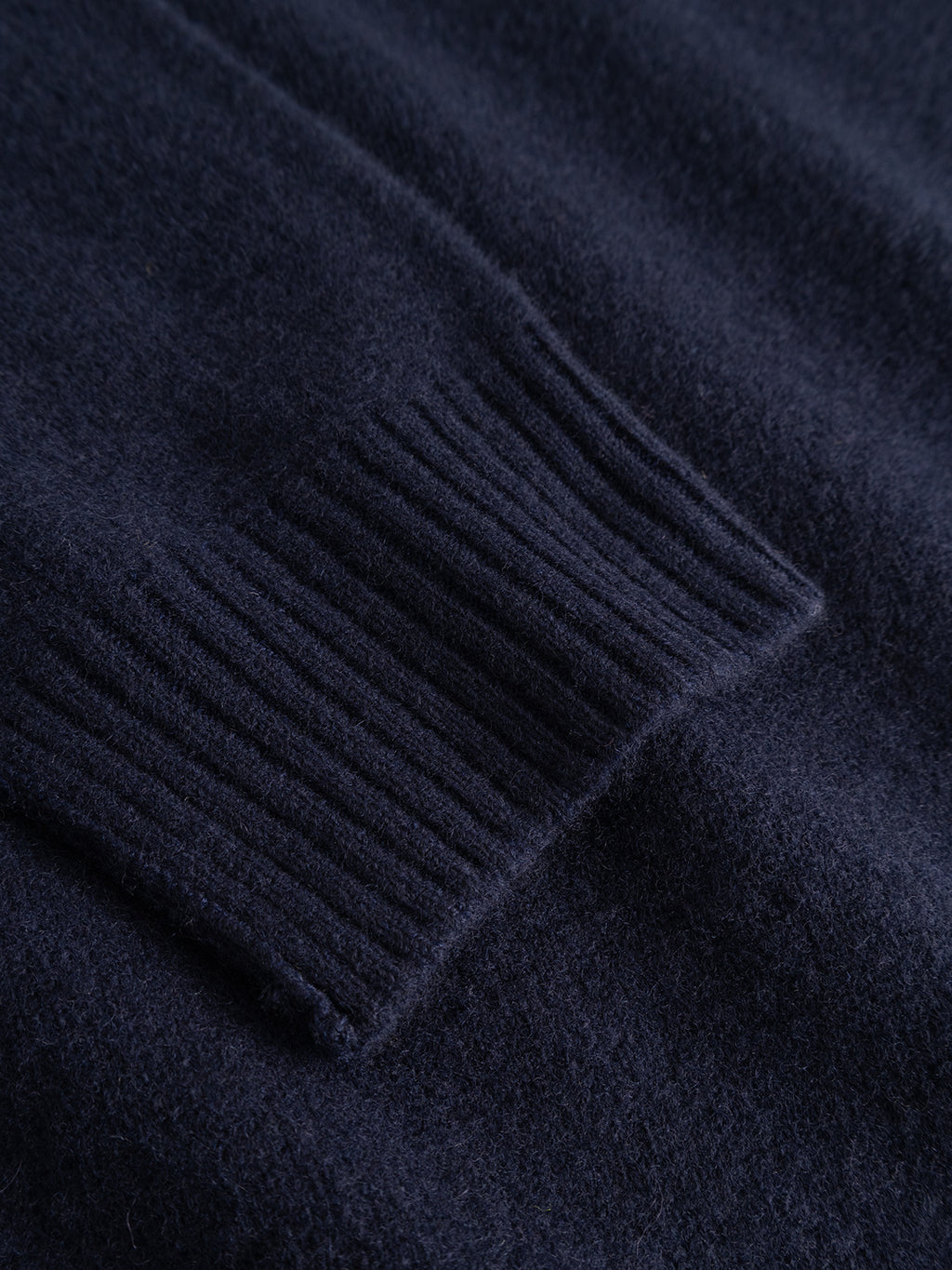 Close-up of the GABtokota Element Aico LS Knit sweater by Gabba in navy, showcasing a soft wool sleeve with fine ribbed cuff detail on textured fabric, designed for everyday comfort.