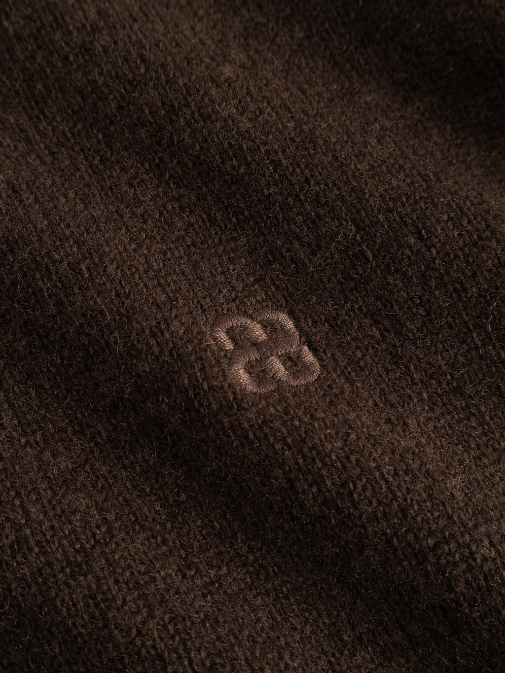 Close-up of the brown slate textured fabric from the Gabba GABtokota Element Aico LS Knit, featuring a small embroidered knot or loop at the center—a detail that hints at decorative stitching or subtle repair, adding unique character and everyday comfort to this favorite crew neck sweater.