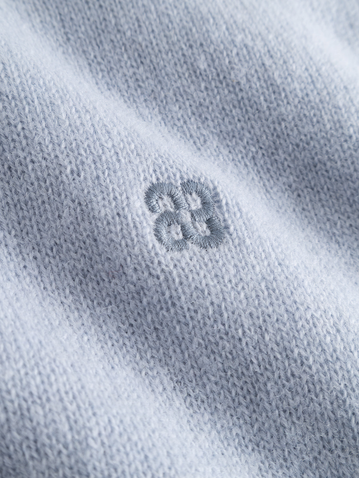 A close-up of the dusty blue knitted fabric from the Gabba GABtokota Element Aico LS Knit sweater, showcasing a soft texture and a delicate, embroidered flower-like pattern with four connected circular shapes at the center—ideal for everyday comfort.