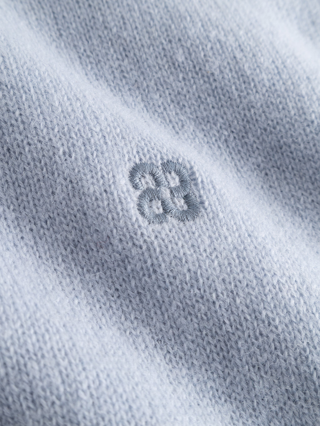 A close-up of the dusty blue knitted fabric from the Gabba GABtokota Element Aico LS Knit sweater, showcasing a soft texture and a delicate, embroidered flower-like pattern with four connected circular shapes at the center—ideal for everyday comfort.