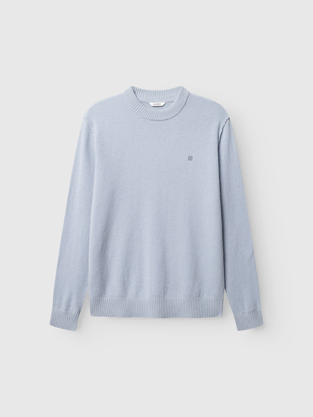 The GABtokota Element Aico LS Knit in Dusty Blue by Gabba is a light blue, long-sleeve crewneck sweater featuring ribbed cuffs, hem, and neckline for everyday comfort. A small, subtle Gabba logo is embroidered on the left chest. This soft wool sweater is shown laid flat against a plain white background.