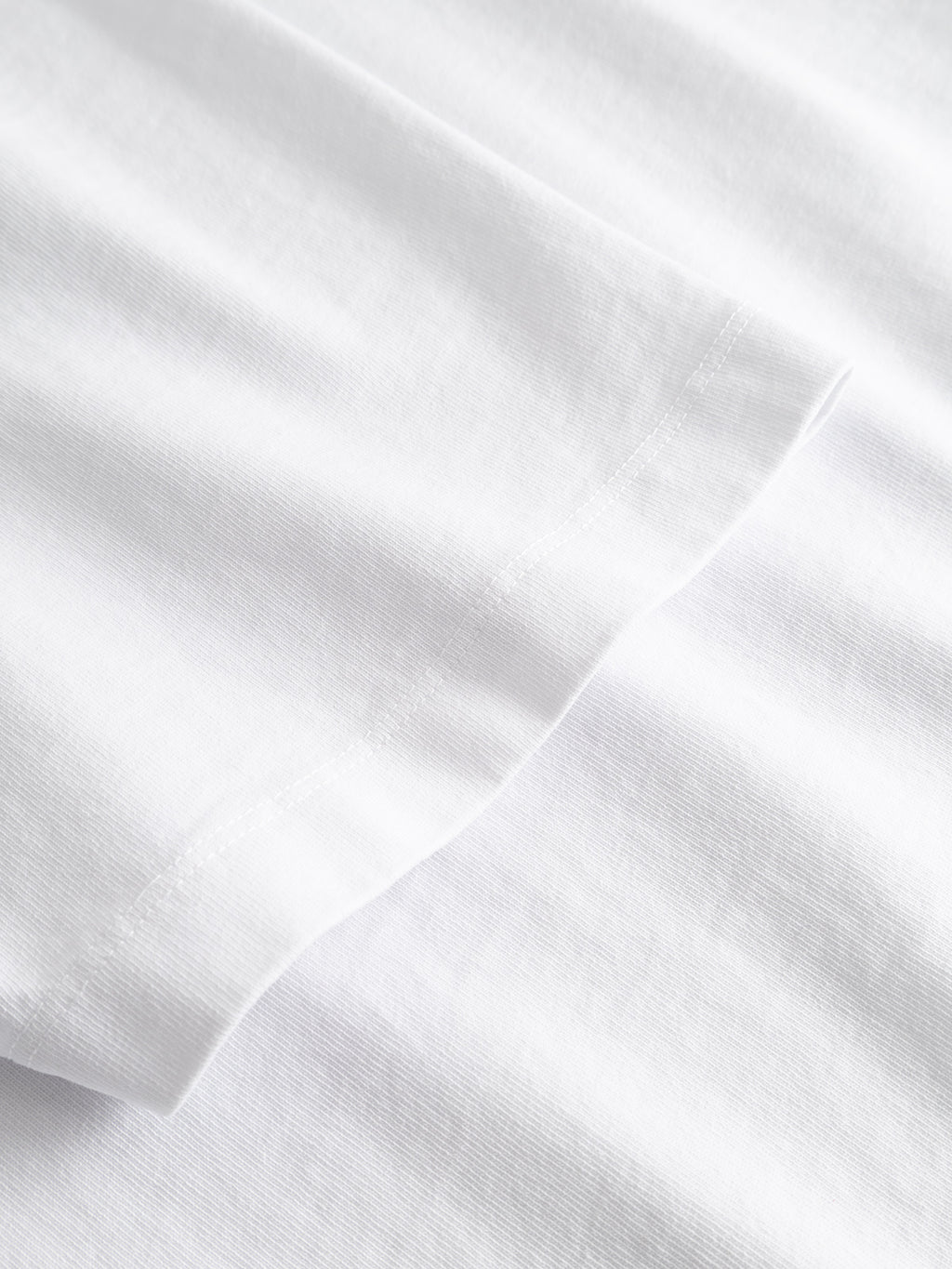 Close-up of the hem and sleeve edge of the Gabba GABlegin Wix Boxy Hour Lobby1 SS T-shirt in White, laid flat to showcase the textured cotton jersey fabric and detailed stitching.