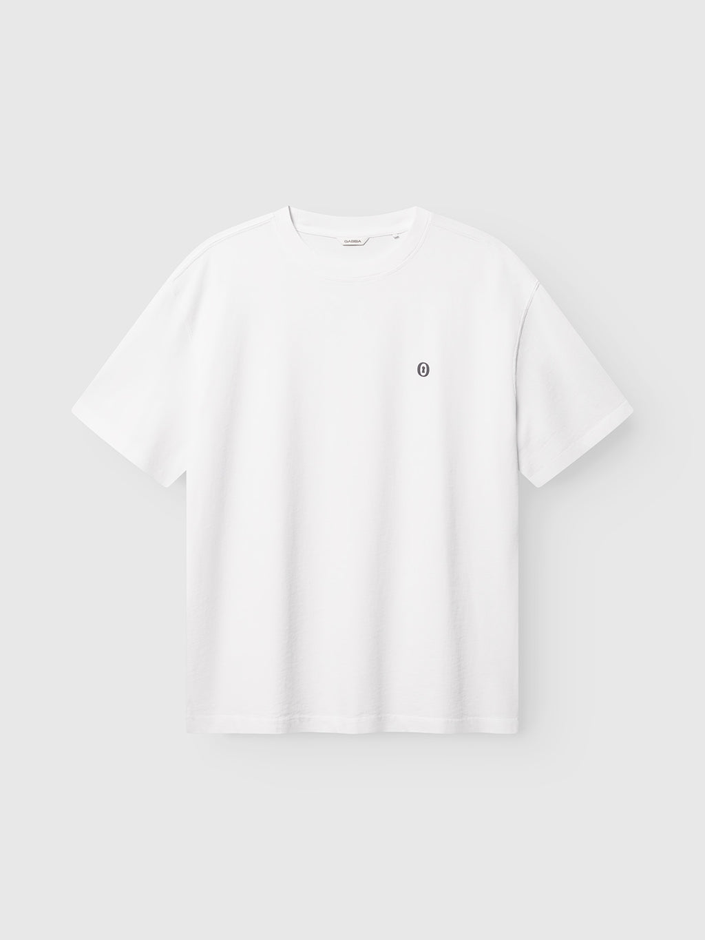 The GABlegin Wix Boxy Hour Lobby1 SS T-shirt by Gabba features a classic plain white design with a small round black and white logo on the left chest, crafted from textured cotton jersey for enhanced depth and comfort, shown against a light gray background.