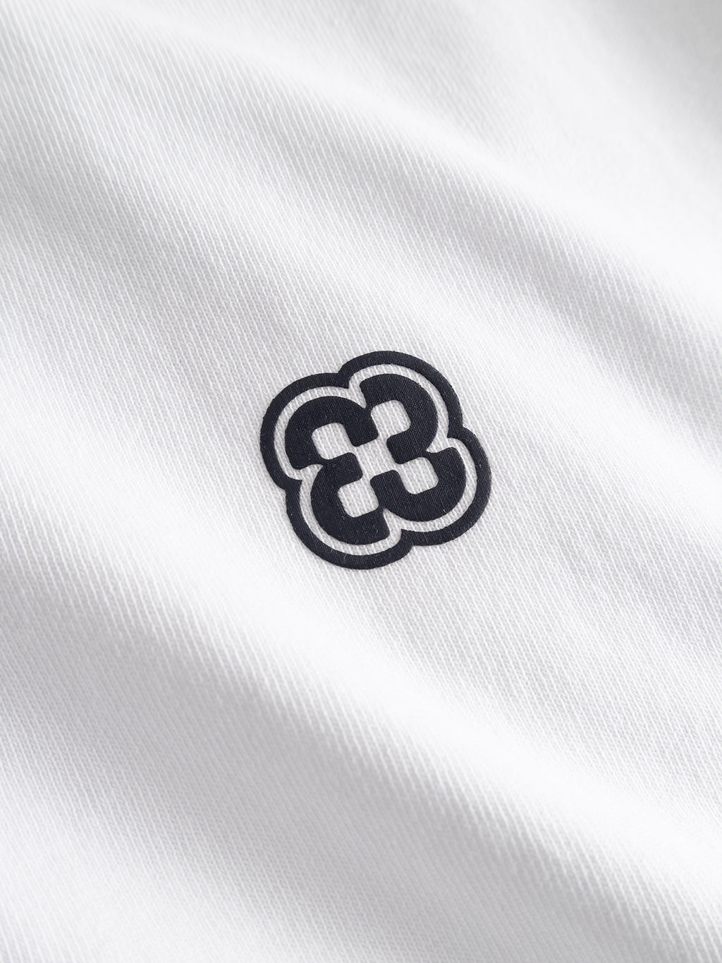 A black geometric clover-shaped design is printed on the white textured cotton jersey of the Gabba GABlegin Wix Boxy Hour Lobby2 SS T-shirt, which features a soft, rippled appearance and a relaxed boxy fit.
