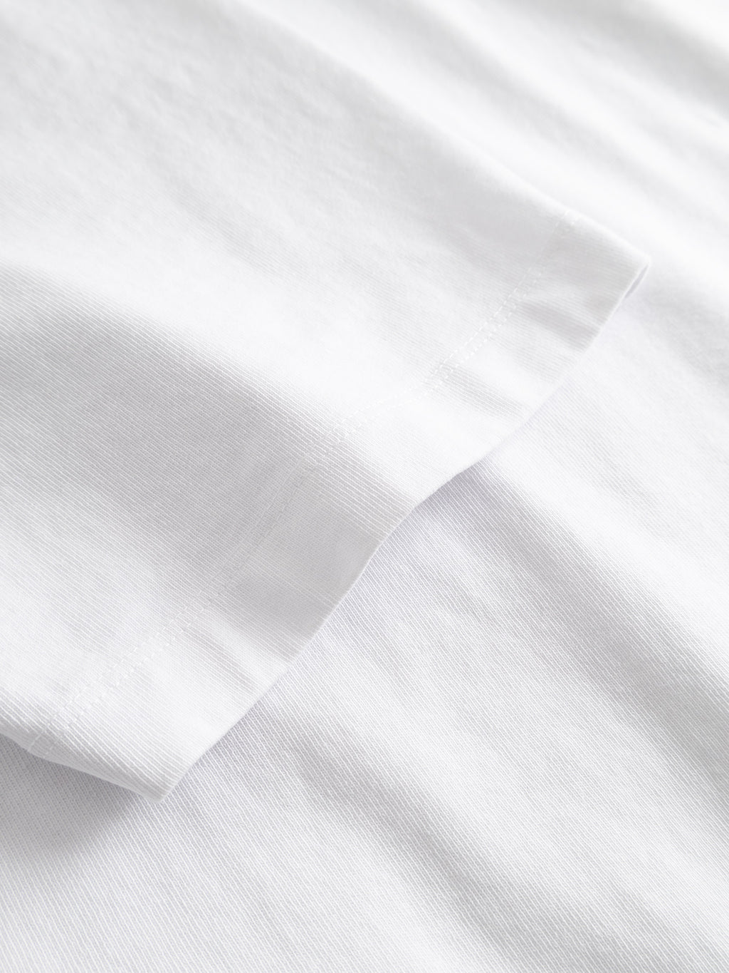 A close-up of a white GABlegin Wix Boxy Hour Lobby2 SS T-shirt sleeve from Gabba, featuring textured cotton jersey fabric, laid flat on a matching white background.