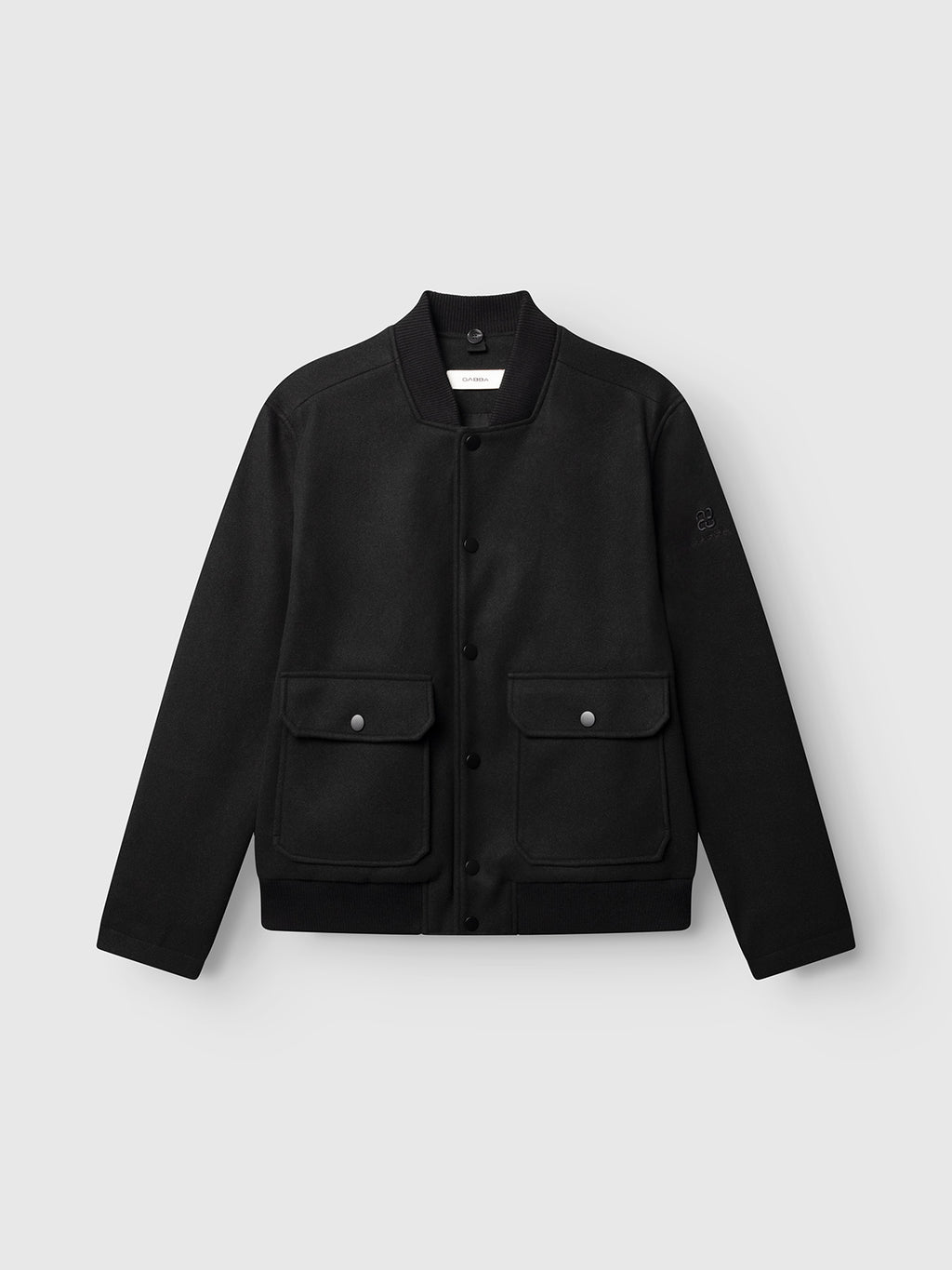 The GABmatheo Plain Bomber Jacket by Gabba in black is crafted from a wool-inspired fabric and features a ribbed collar, snap button closure, and two spacious front flap pockets—making it the perfect casual outer layer. Shown here against a plain light gray background.