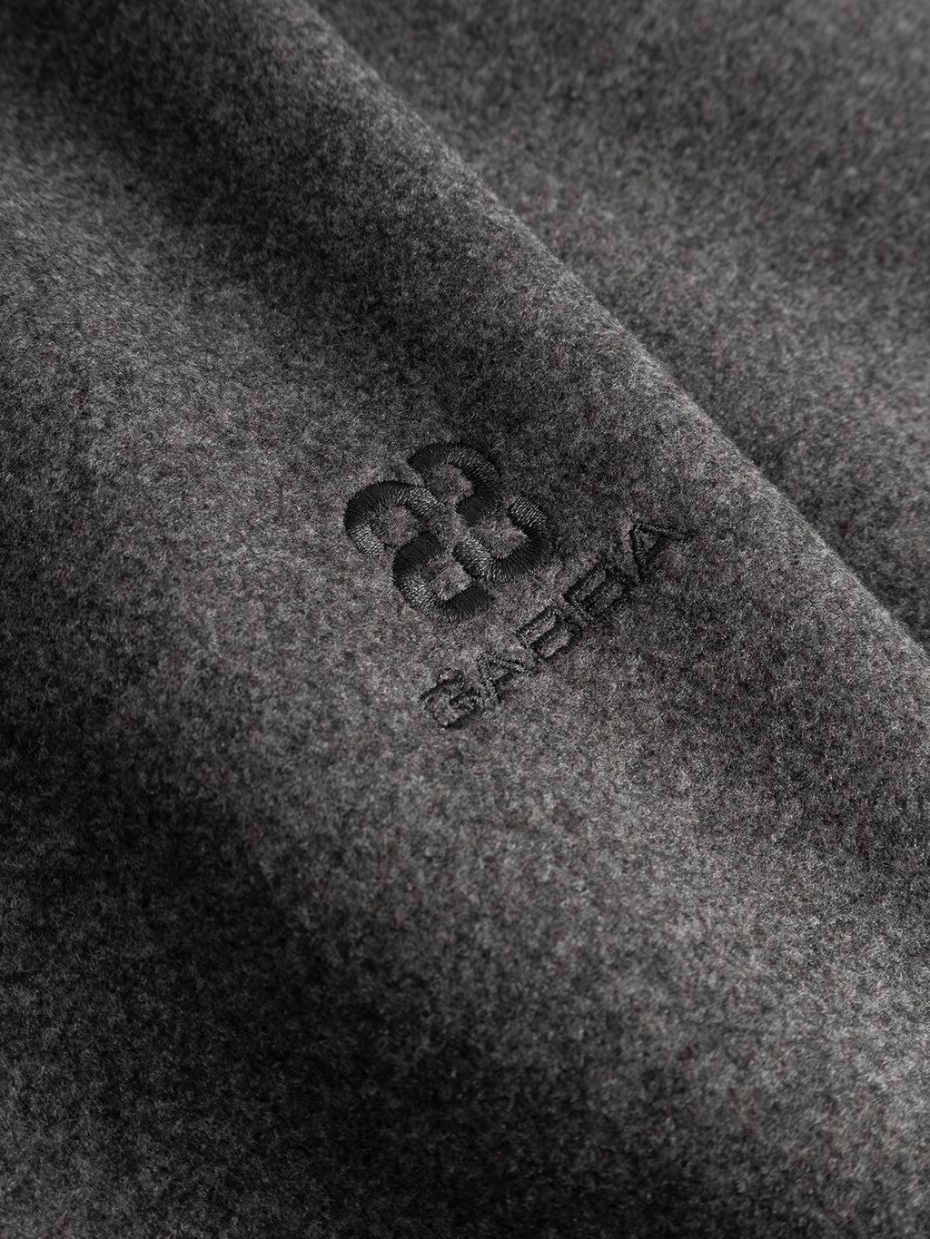 A close-up of the dark grey GABtheo City Jacket from Gabba, featuring wool-inspired fabric with the Gabba name and a stylized B logo embroidered in dark thread—ideal for everyday layering or as an elegant overshirt jacket.