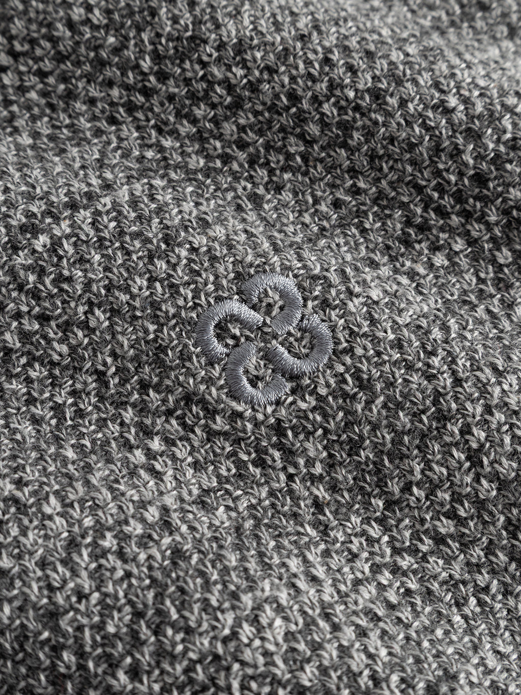 Close-up of the GABlamix Coro O-Neck LS Knit by Gabba in light grey, highlighting the cotton-blend fabric and its textured knit, with a subtle embroidered knot-like design at the center.