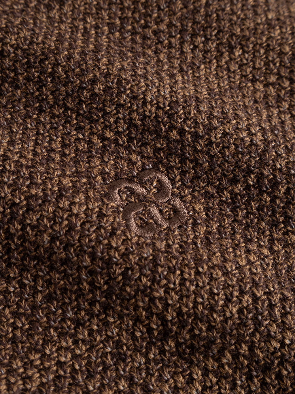 Close-up of the Gabba GABlamix Coro O-Neck LS Knit in Brown Slate, showcasing its dark brown cotton-blend knit fabric with a centrally embroidered ampersand symbol in matching brown thread.