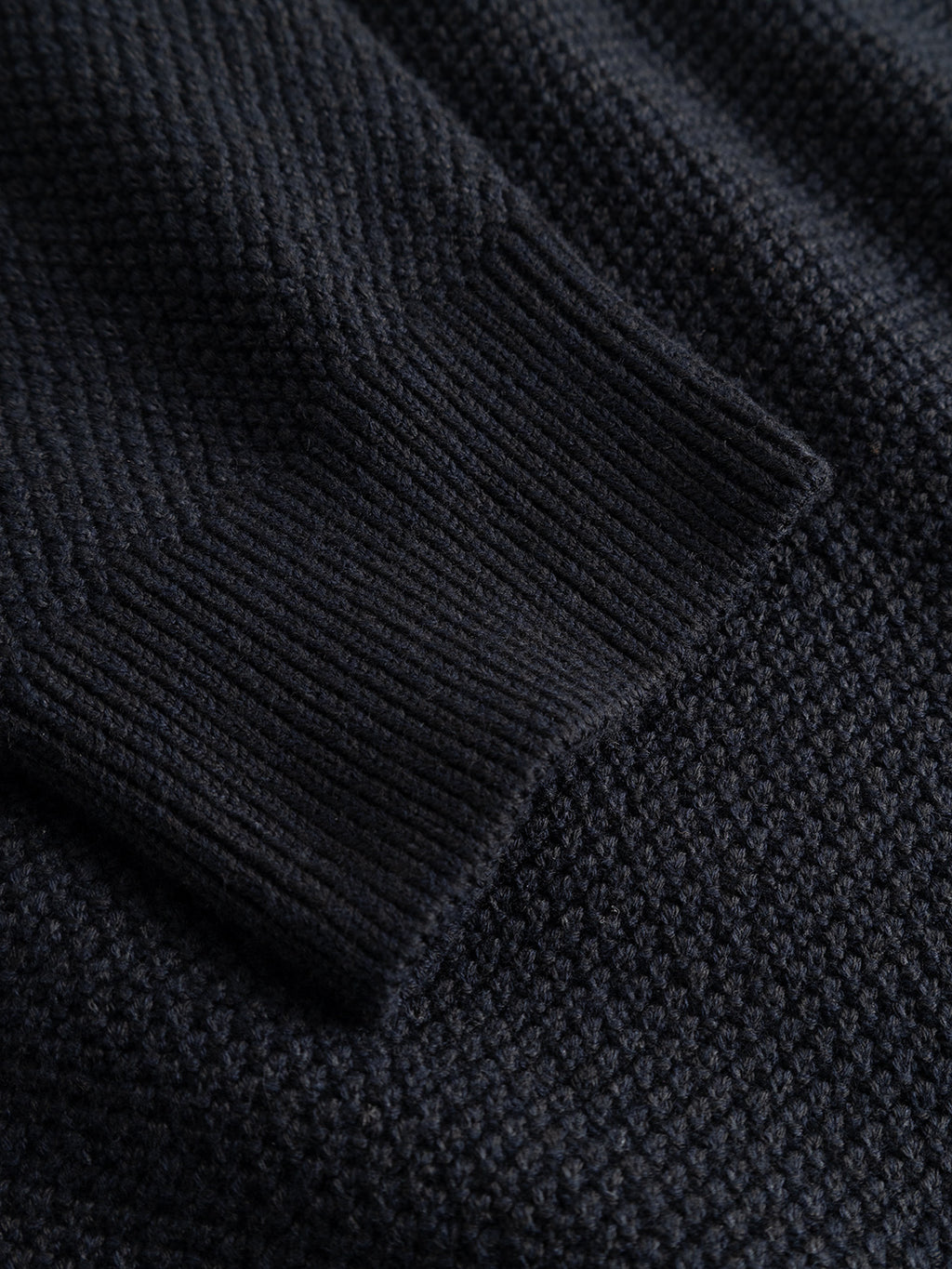 Close-up of the “GABlamix Coro O-Neck LS Knit - Blue Black” sweater by Gabba, highlighting the cuff of the sleeve and the textured cotton-blend knit fabric. This regular fit crew neck sweater exemplifies detailed craftsmanship and timeless style.