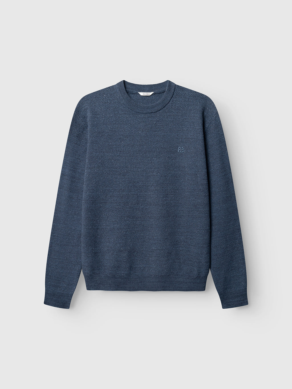 The Gabba GABlamix Coro O-Neck LS Knit in Turbulence Blue is a textured cotton-blend sweater with long sleeves and a classic crew neck, showcased against a light gray background. A small embroidered Gabba logo accents the left chest area.