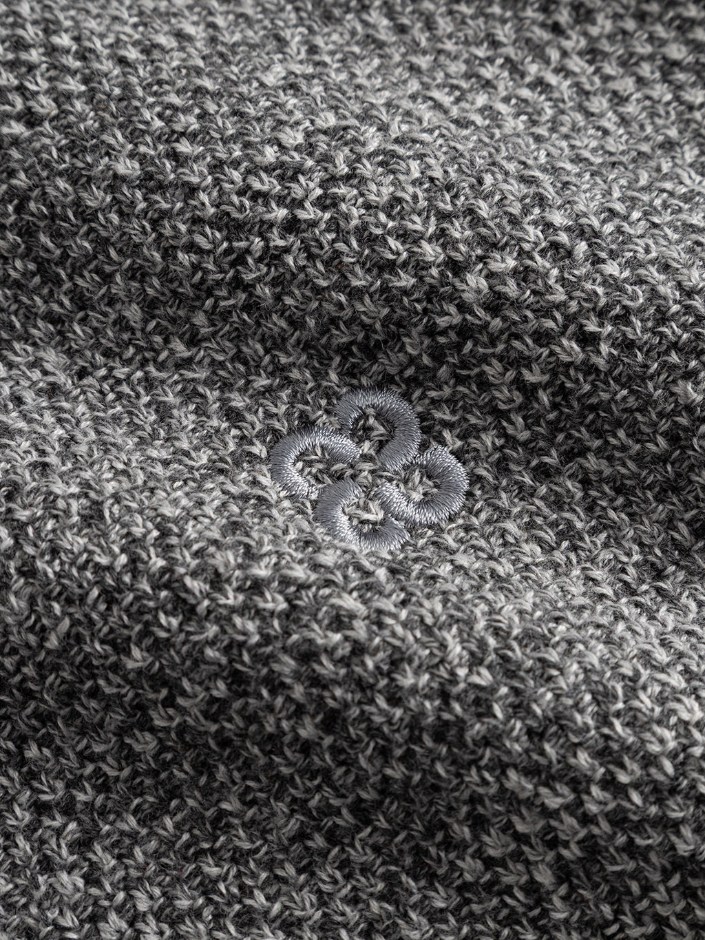 Close-up of the textured light grey cotton-blend knit fabric from the Gabba GABlamix Coro Half LS Knit, featuring a small embroidered flower motif at the center. The soft and substantial material suggests it is part of a regular fit sweater.