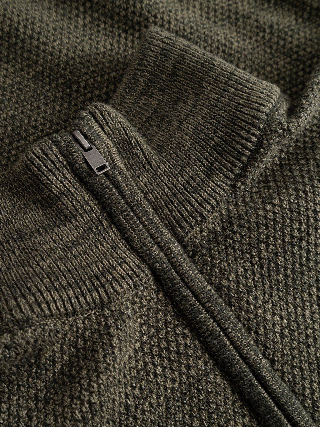 Close-up of the Gabba GABlamix Coro Half LS Knit in Forest Night, a textured dark green cotton-blend sweater featuring a ribbed collar and a partially unzipped black metal zipper diagonally set across the fabric, highlighting its regular fit.