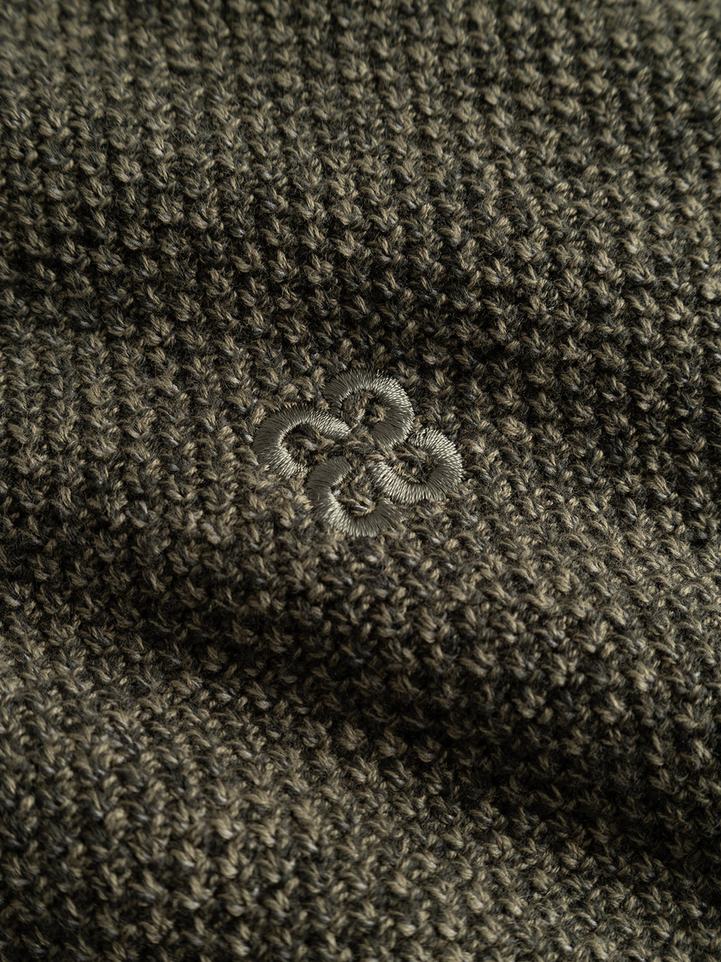 Close-up of the Gabba GABlamix Coro Half LS Knit in Forest Night, featuring a textured dark cotton-blend knit fabric with a small, intricate embroidered flower design at the center.