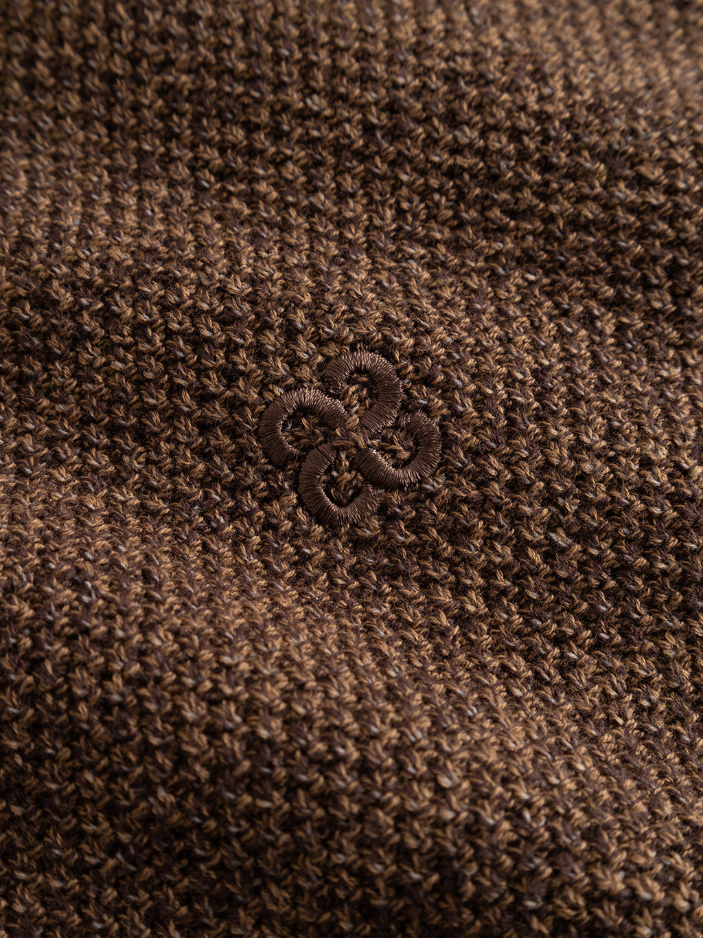 Close-up of the GABlamix Coro Jhon LS Knit in Brown Slate—a cotton-blend knit fabric by Gabba—showcasing its textured pattern, an embroidered circular decorative design at the center, and a subtle Gabba brand mark.