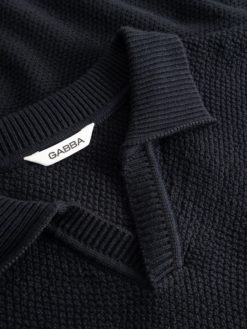 Close-up of the GABlamix Coro Jhon LS Knit in Blue Black by Gabba, featuring a refined textured knit with a ribbed collar, partially folded open to reveal a white Gabba label.