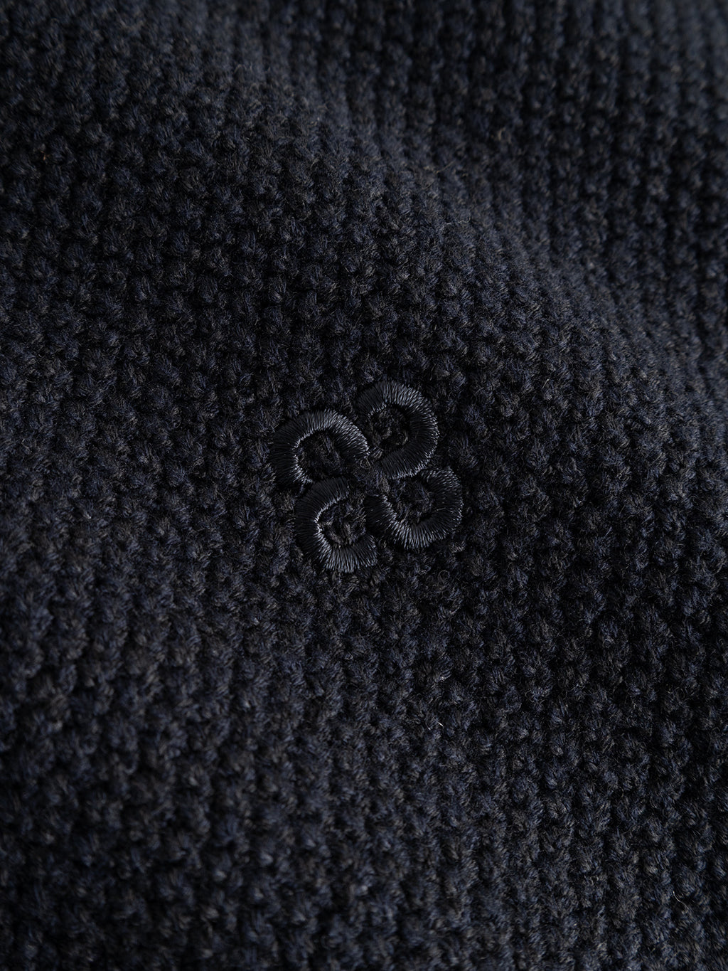 Close-up of the Gabba GABlamix Coro Jhon LS Knit in Blue Black, featuring textured dark cotton-blend knit fabric and a subtle, small embroidered geometric design with four curved, looped shapes at the center.