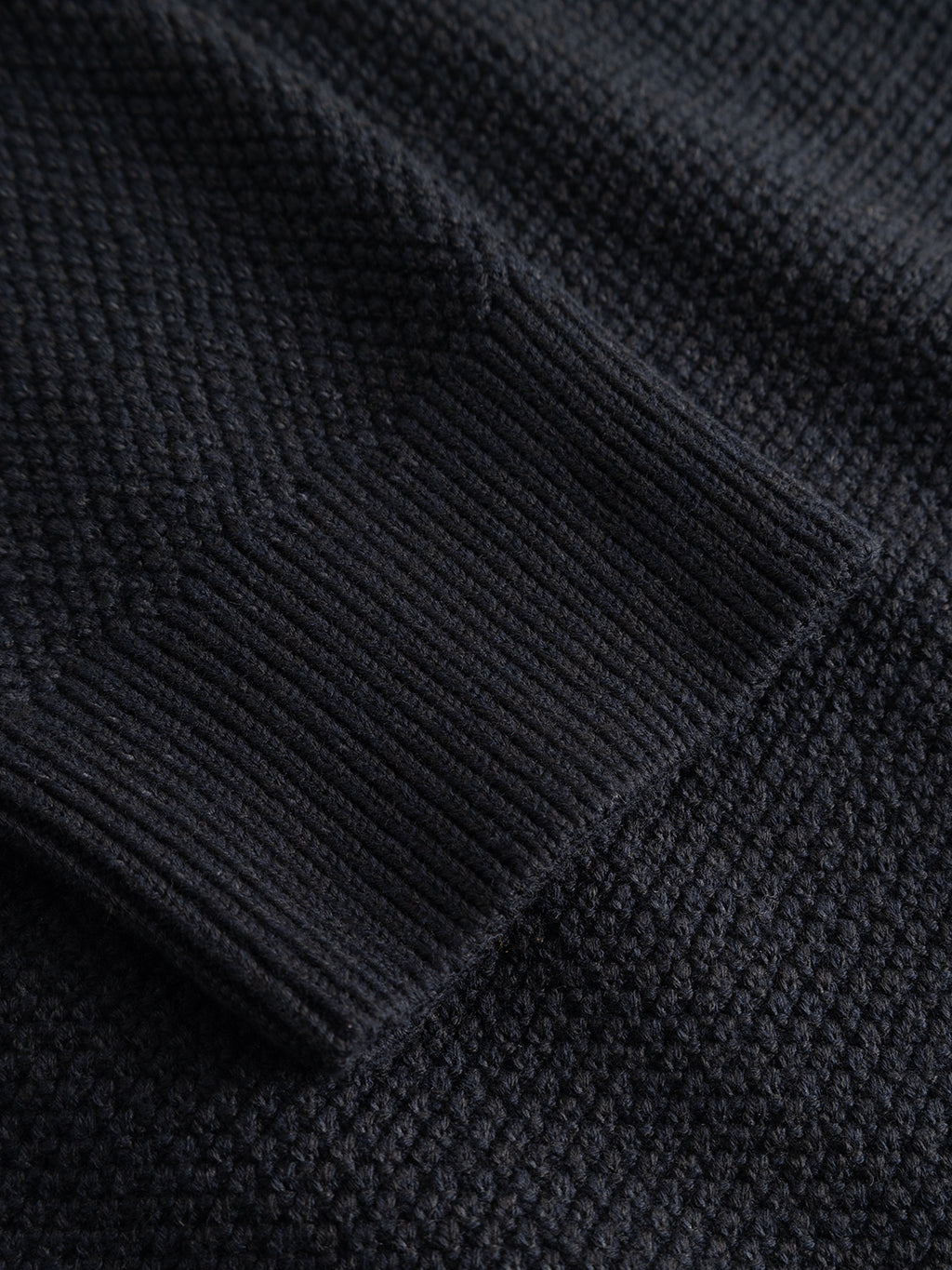 Close-up of the Gabba GABlamix Coro Jhon LS Knit in Blue Black, highlighting its dark, textured cotton-blend knit fabric and ribbed cuff, with fine detailing visible in the refined weave as it lies flat.