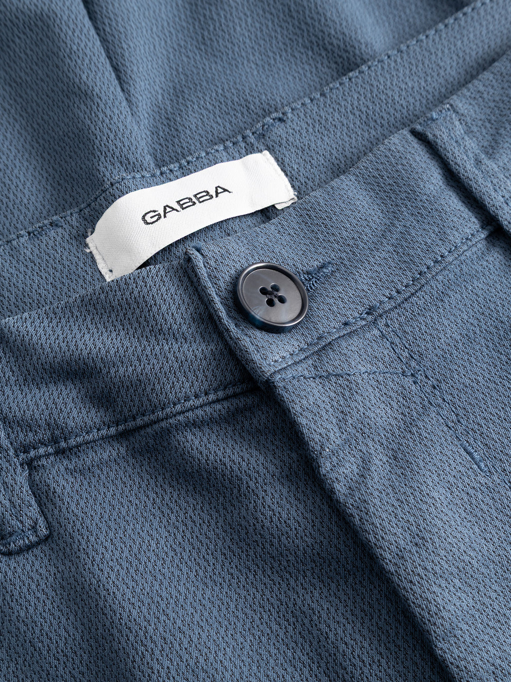 Close-up of the blue GABpaul K3280 Dale Chino - Bering Sea by Gabba, featuring textured slim fit, dark button, French pockets, belt loop, and a white inner label with Gabba branding in black.