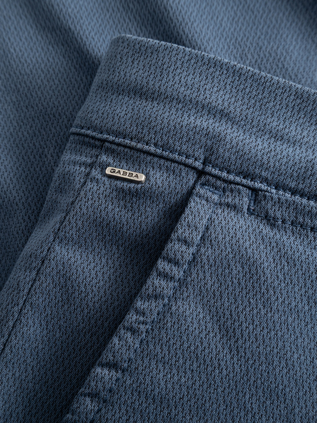 Close-up of the GABpaul K3280 Dale Chino in Bering Sea by Gabba, showing its blue textured fabric, classic French pockets, a branded metal tag above the pocket, and a modern slim leg opening.