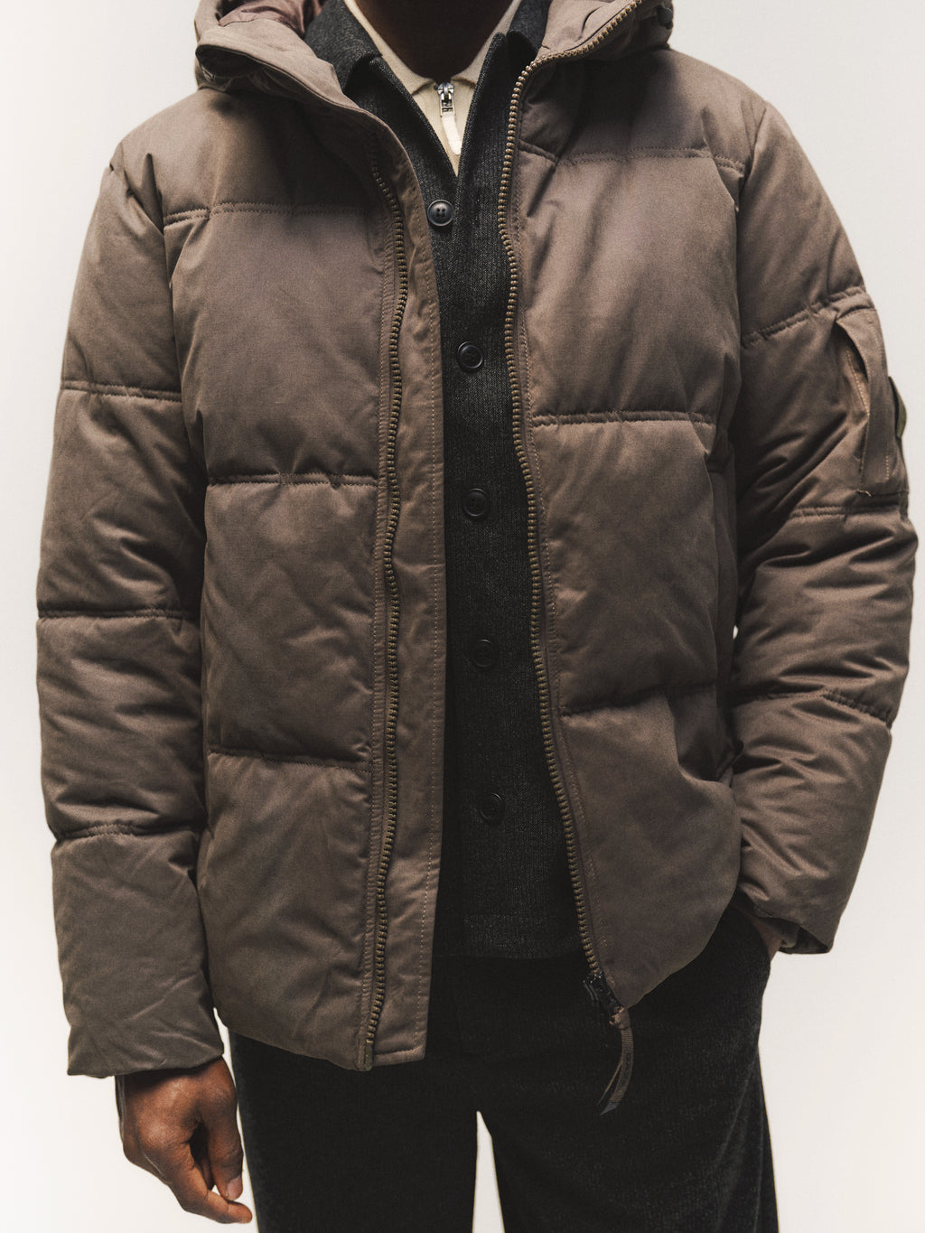A person wearing a brown GABjulien Calle Outerwear - Brown Slate hooded puffer jacket over a dark button-up sweater.