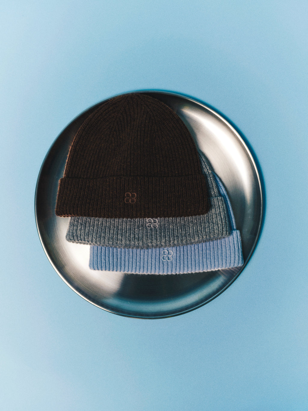 Three GABeast Flash Beanies in Grey Mel by Gabba are neatly stacked on a round silver tray against a light blue background, offering the perfect winter accessory for staying warm.