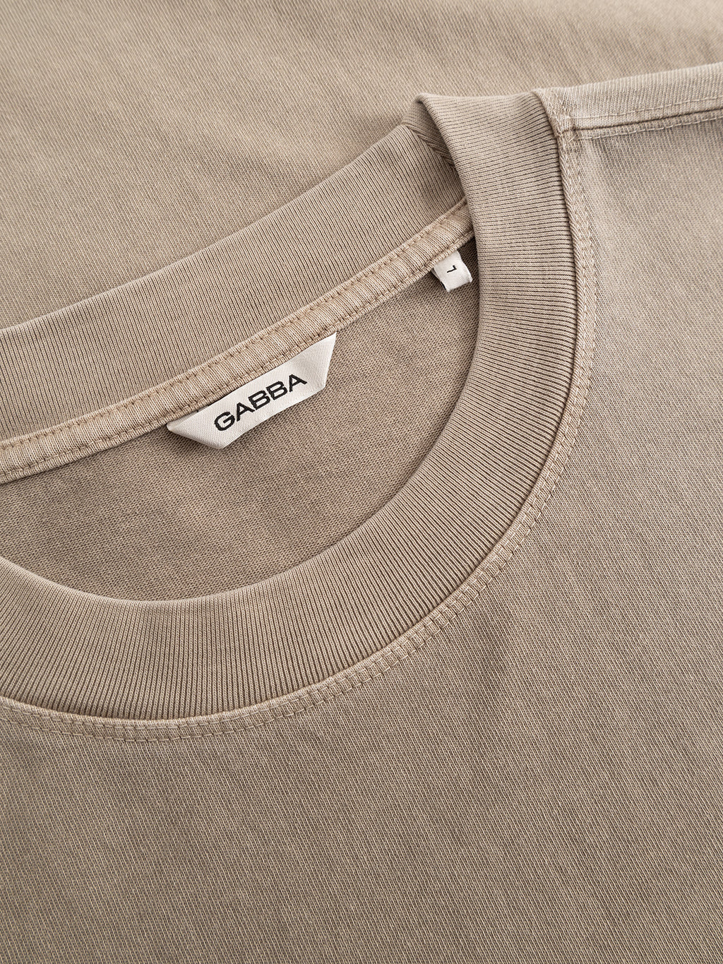Close-up of the Gabba GABlegin Wix Boxy Hour SS T-shirt in Sand Crocker, highlighting the visible Gabba label at the crewneck. Made from mid-weight cotton jersey, the image clearly showcases the fabric texture and stitching details. This design offers a relaxed boxy fit for enhanced comfort.