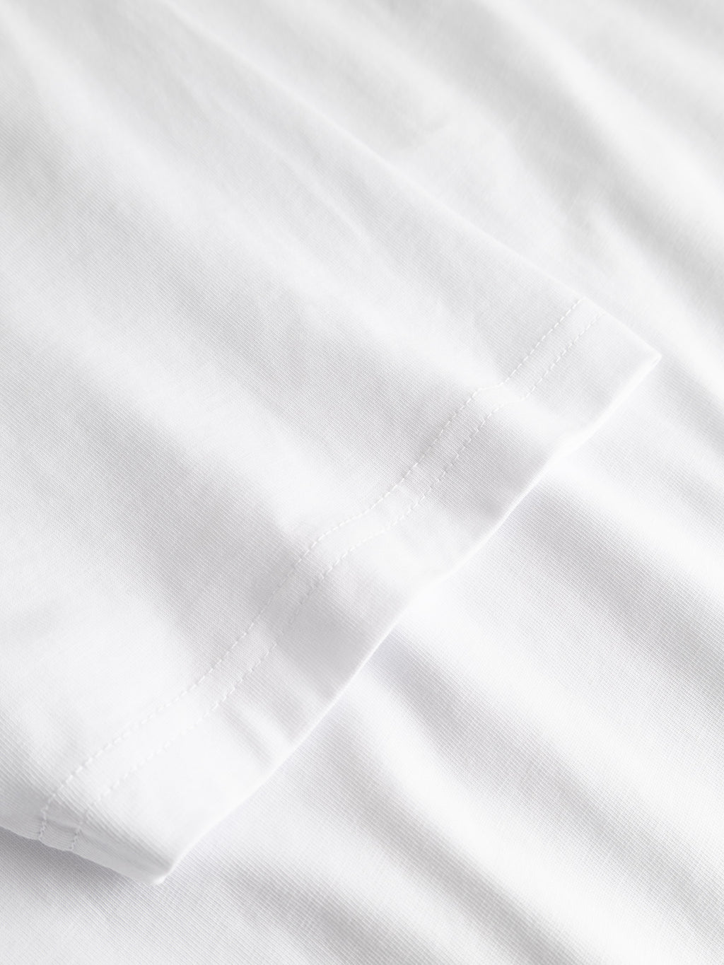 Close-up of the edge and stitching detail of the GABdune Element GOTS SS T-Shirt in white by Gabba, featuring smooth organic cotton fabric on a white background.