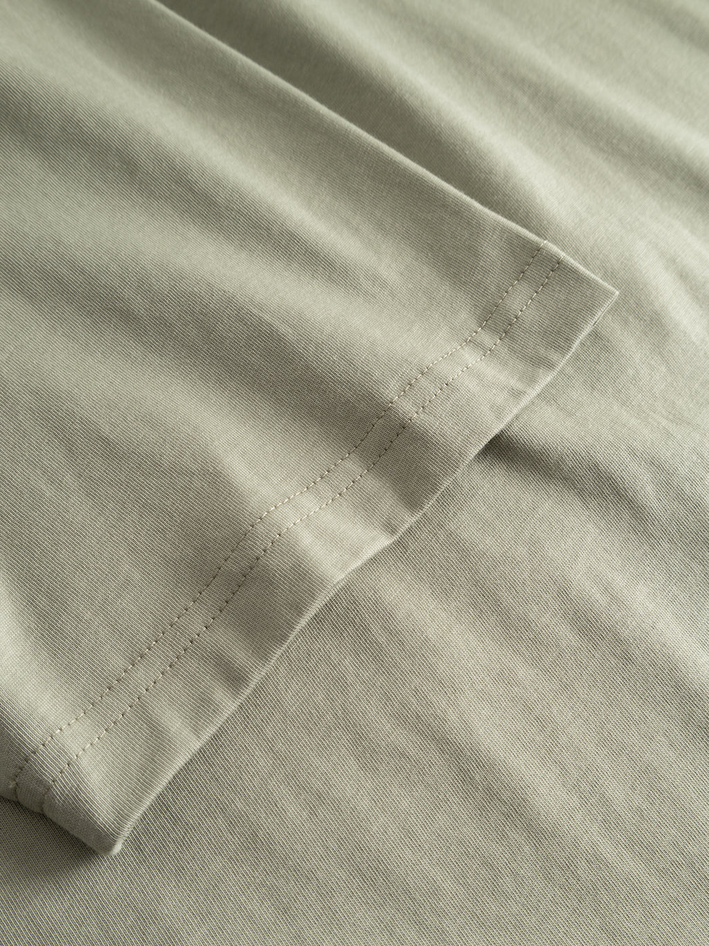 Close-up of the Gabba GABdune Element GOTS SS T-Shirt in light green, highlighting the hem and sleeve stitching details of this classic fit organic cotton tee, GOTS-certified and laid flat on a matching surface.