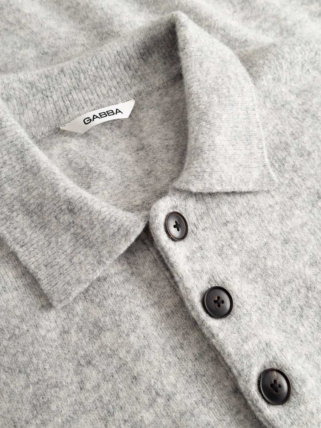 Close-up of the GABpietro Polo Argyle LS Knit in Lt. Grey Mel by Gabba, featuring a light gray wool-textured collared design with three dark buttons and a visible white Gabba label, highlighting its modern silhouette sweater style.