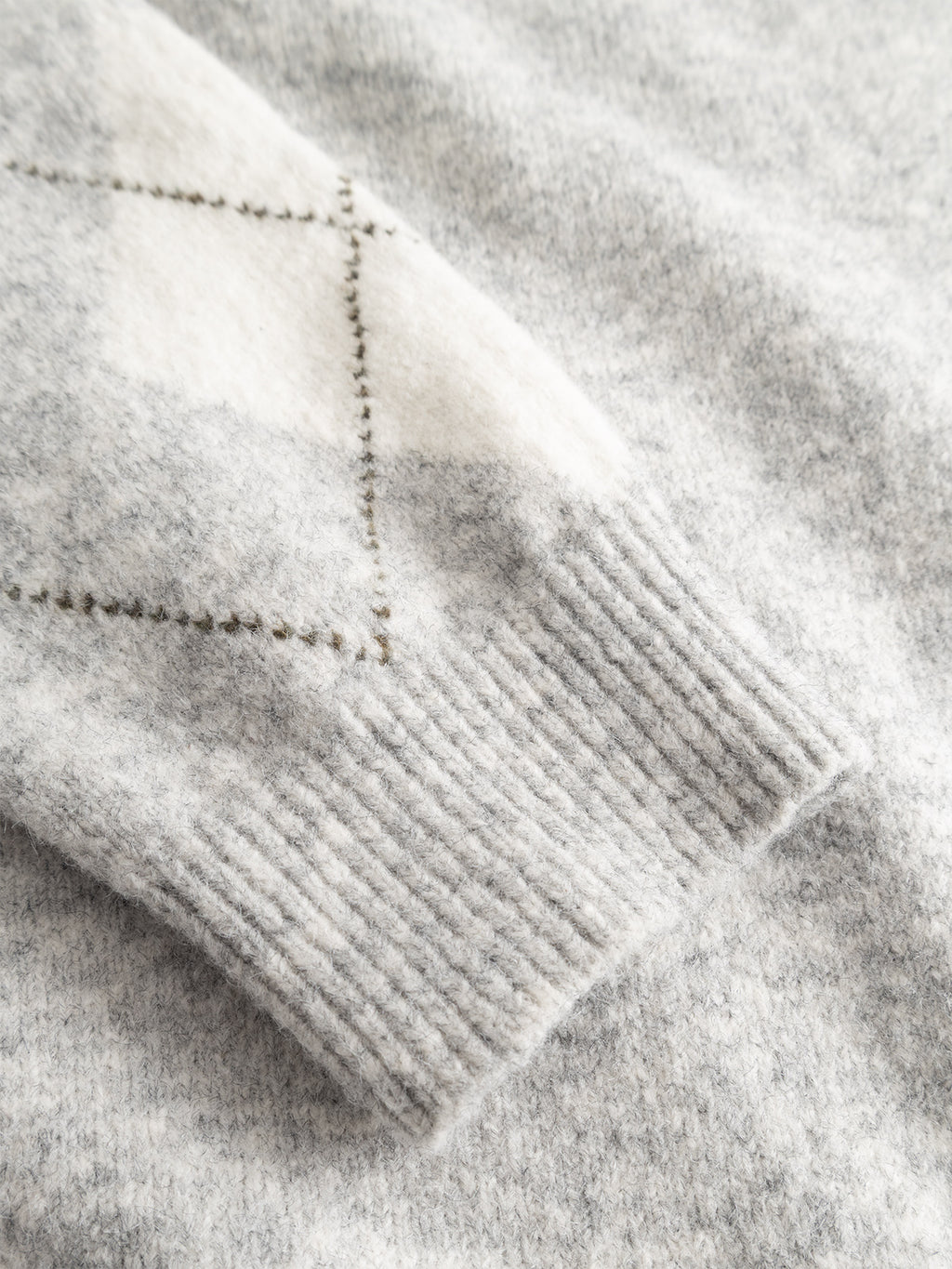 A close-up of the GABpietro Polo Argyle LS Knit in Lt. Grey Mel from Gabba highlights the ribbed knit texture and white and dark grey argyle pattern on the sleeve. This modern silhouette sweater features a boxy fit knit, offering both comfort and contemporary style.