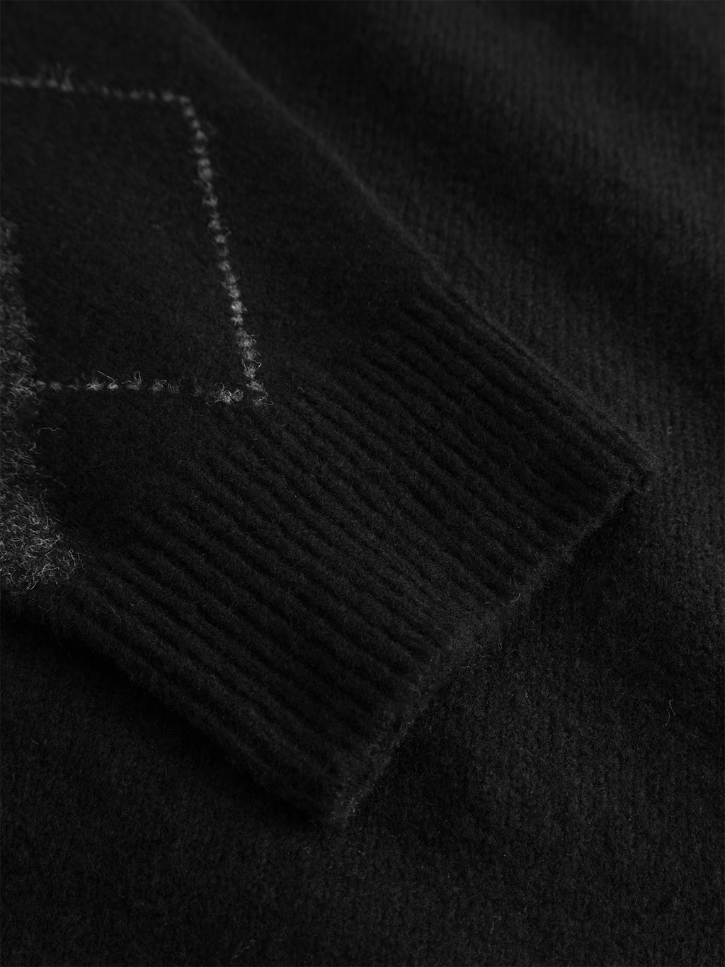 A close-up of the Gabba GABpietro Polo Argyle LS Knit in black highlights its ribbed cuff and subtle argyle pattern, showcasing the contemporary knit texture and boxy, relaxed fit.