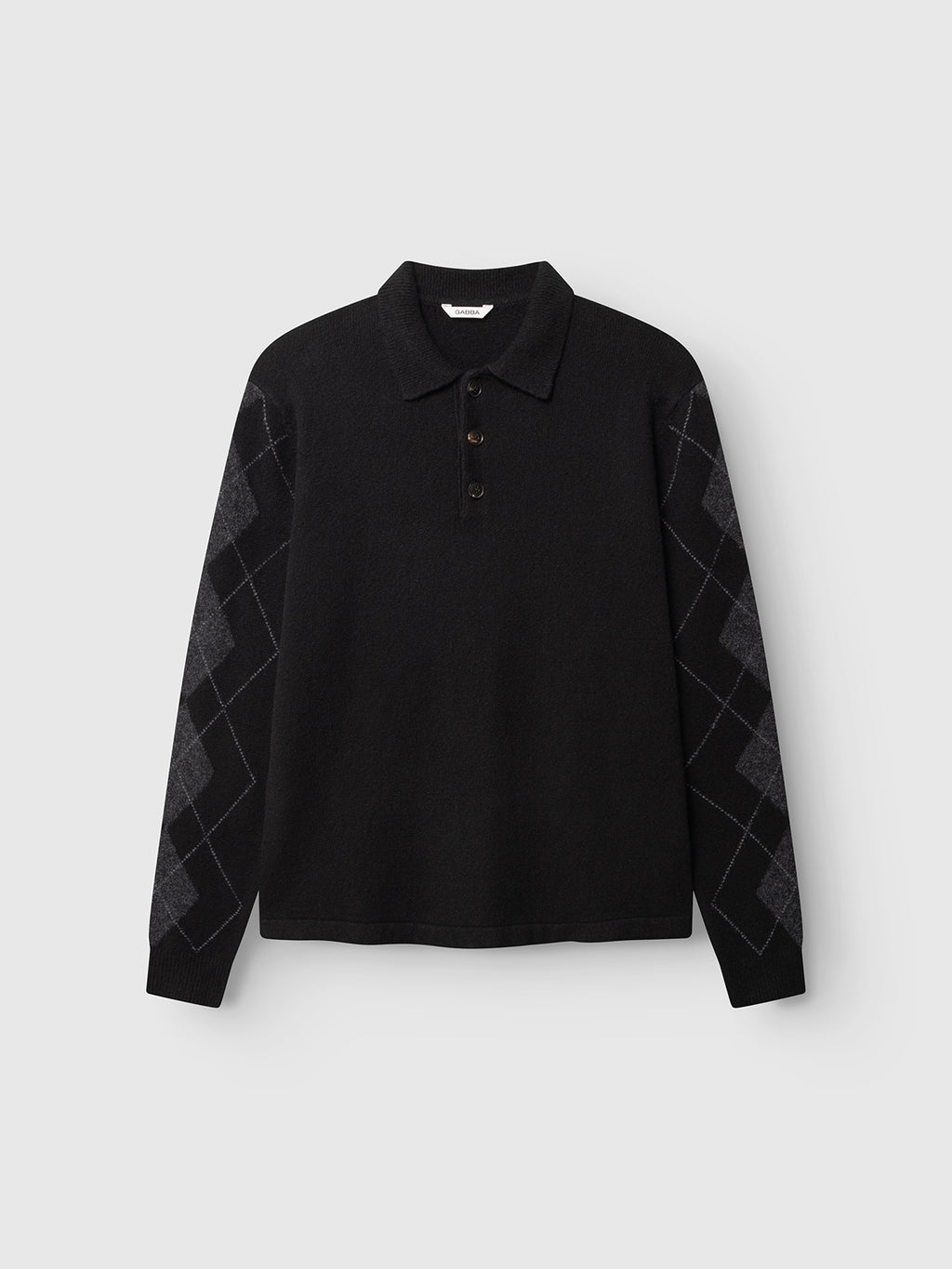 The Gabba GABpietro Polo Argyle LS Knit in black is a long-sleeve cotton blend polo shirt featuring a collar, three-button placket, and gray diamond argyle patterns on the sleeves. With its boxy, relaxed fit and contemporary knit design, it is shown against a plain light gray background.