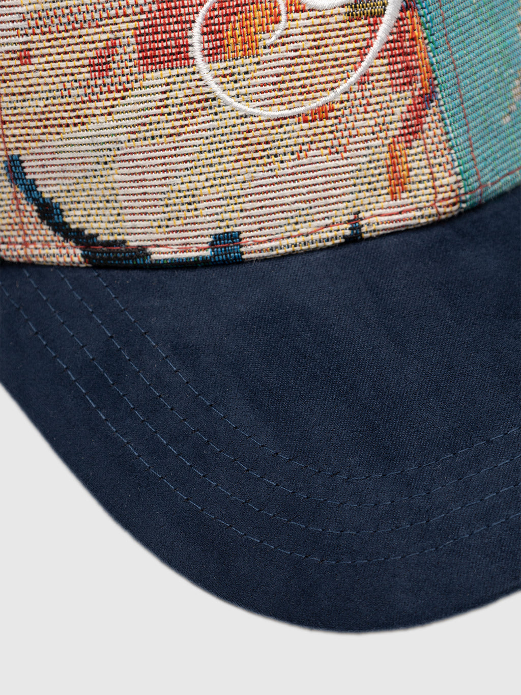 Close-up of the GABrichi Fiore Cap - Multi Pattern by Gabba, showcasing its textured jacquard multicolored fabric panel and solid navy blue curved brim. Visible stitching and an embroidered Gabba logo adorn the upper section, while an adjustable back strap ensures a customized fit.