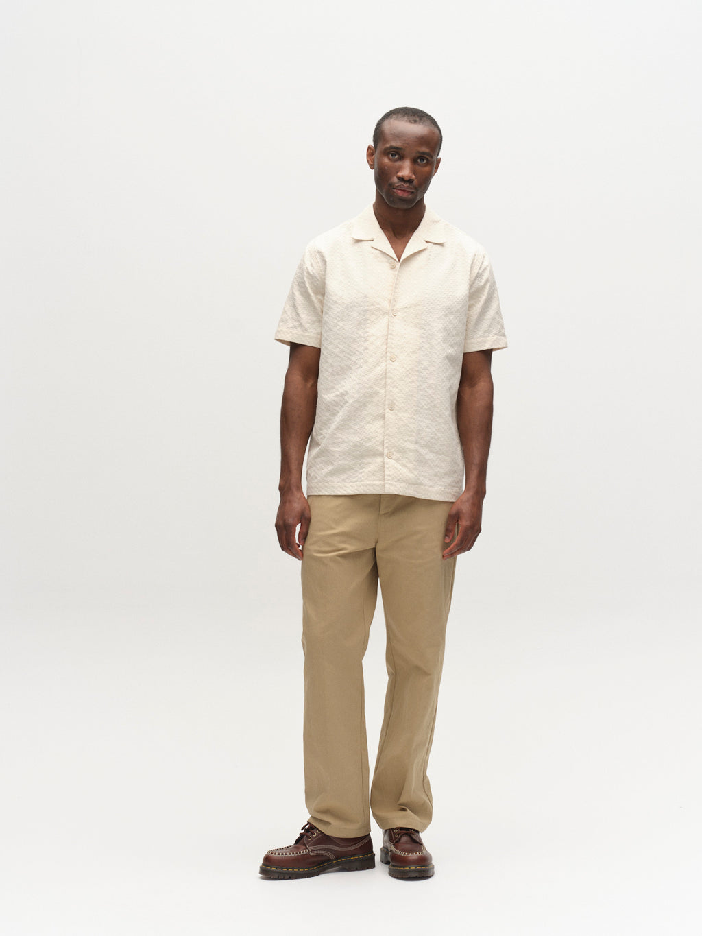 A man stands against a plain white background, wearing the Gabba GABtimo Resort Neal SS Shirt in Birch, tan pants, and brown shoes. He faces forward with a relaxed posture and a neutral expression.