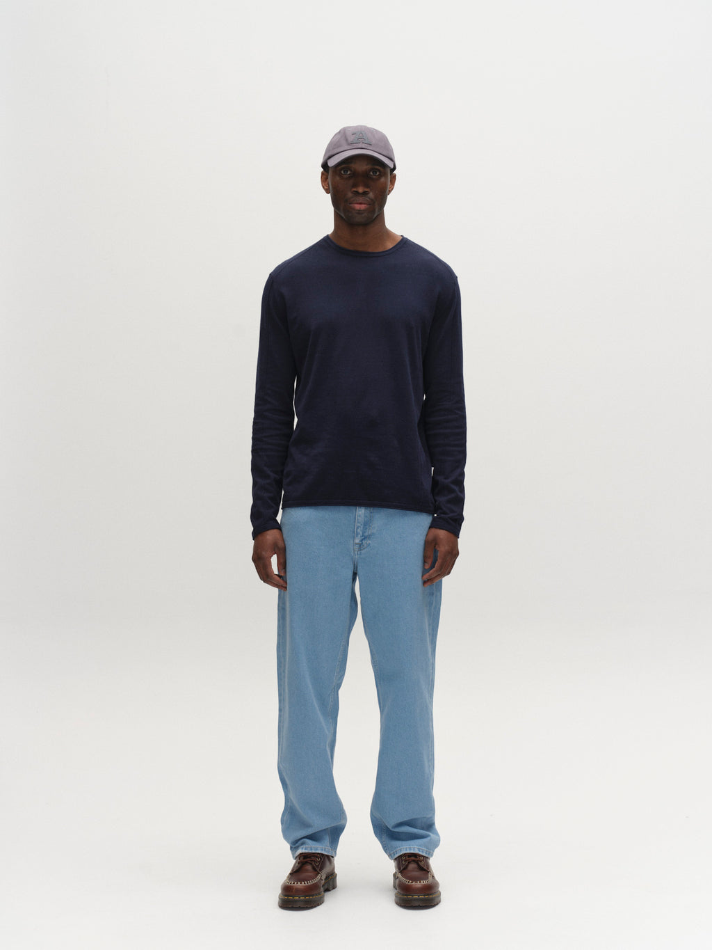 A man stands against a white background, wearing a gray cap, dark long-sleeve shirt, brown shoes, and Gabba GABmax 5poc Lig Jeans in light blue denim. He faces forward with his arms relaxed at his sides.