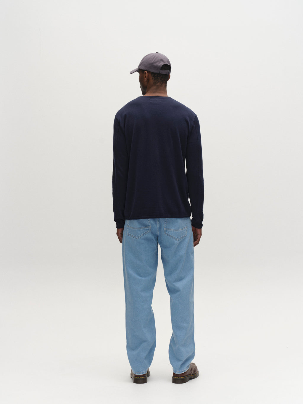 A man faces away from the camera, wearing a gray cap, navy long-sleeve shirt, brown shoes, and Gabba GABmax 5poc Lig Jeans in Lt. Blue Denim, standing against a plain white background.