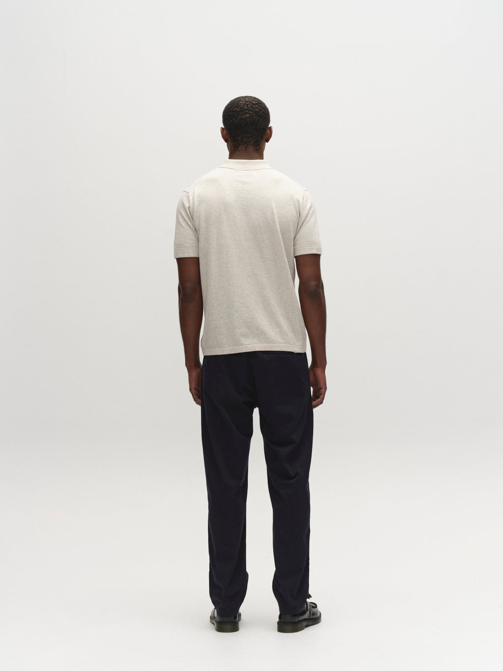 A man stands facing away from the camera in a plain, light-colored short-sleeve shirt, Gabba GABjoe Nopleats Dale Pant in Blue Black, and black shoes against a simple white background.
