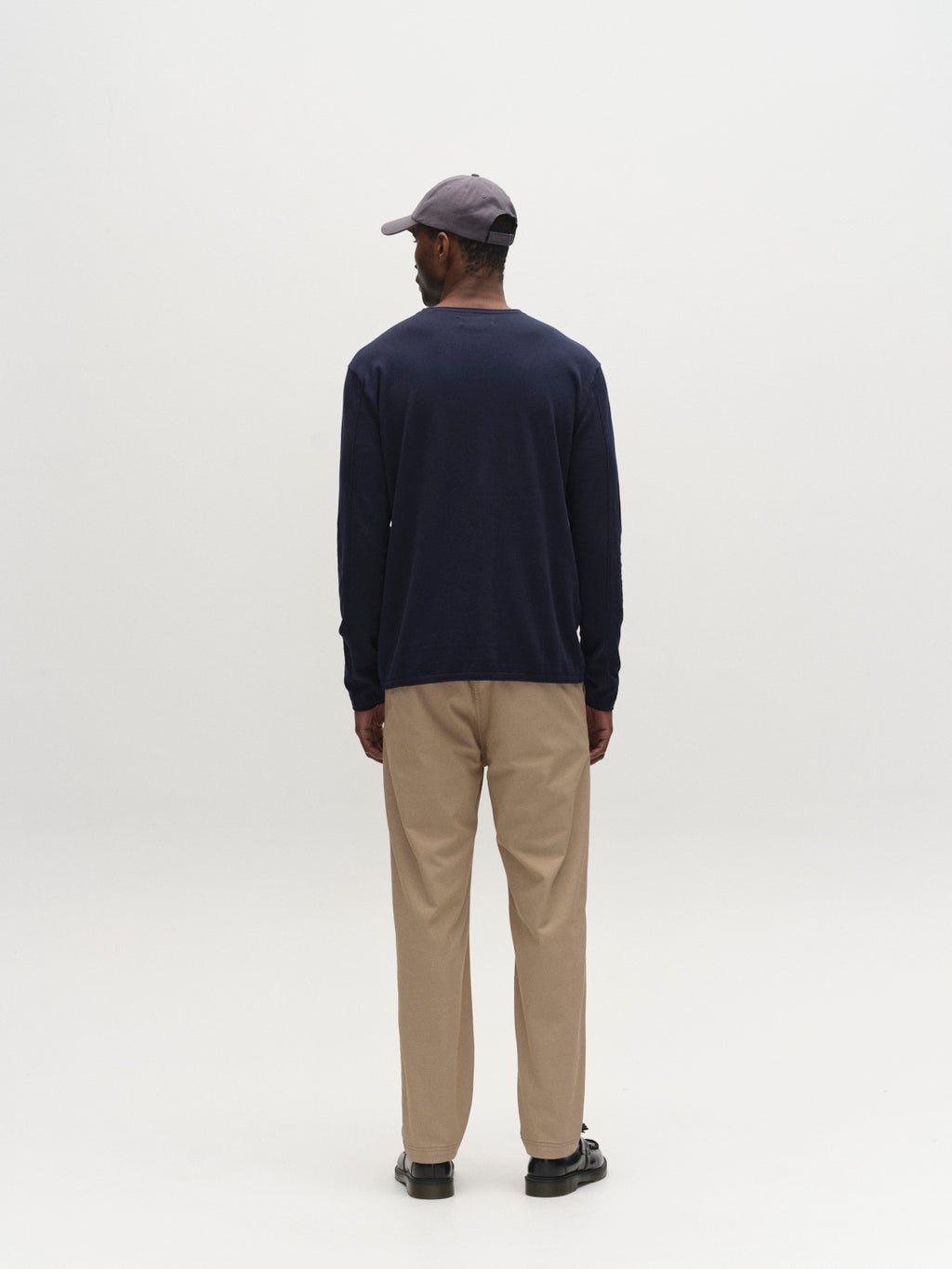 A man faces away from the camera, wearing the Gabba GABlima Cot LS Knit - Navy shirt with beige pants and dark shoes, set against a plain white background.