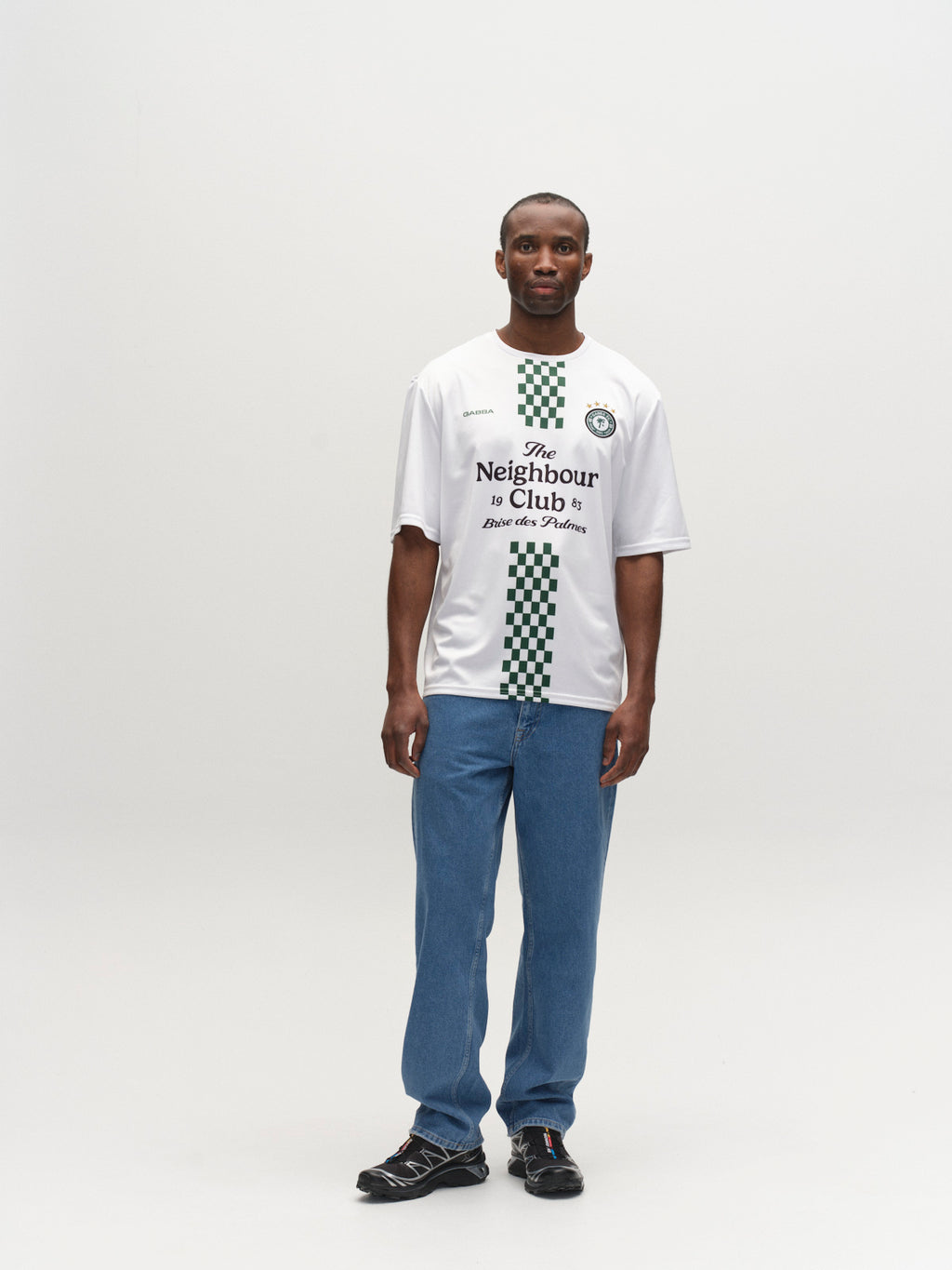 A man stands facing the camera, wearing the Gabba GABnigel Fut Boxy Pes SS T-shirt in white, paired with blue jeans and black shoes, against a plain white background.