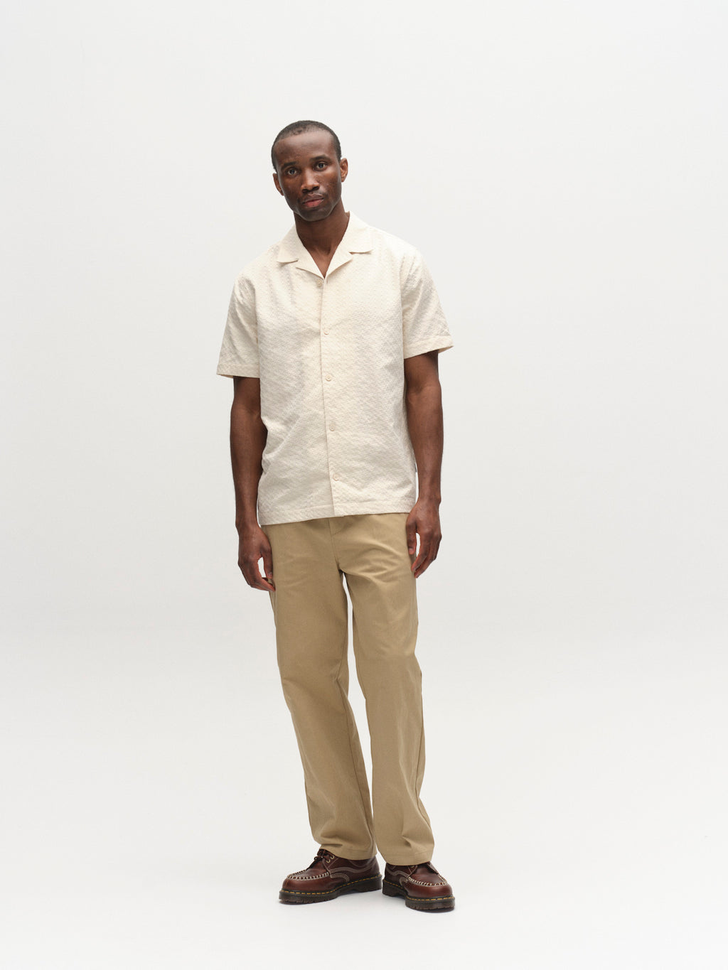 A man stands against a white background, wearing a light beige shirt and Gabba GABdenver Fuggies Pant in Sand. His posture is relaxed, he faces forward, and his expression is neutral. He also wears brown shoes.