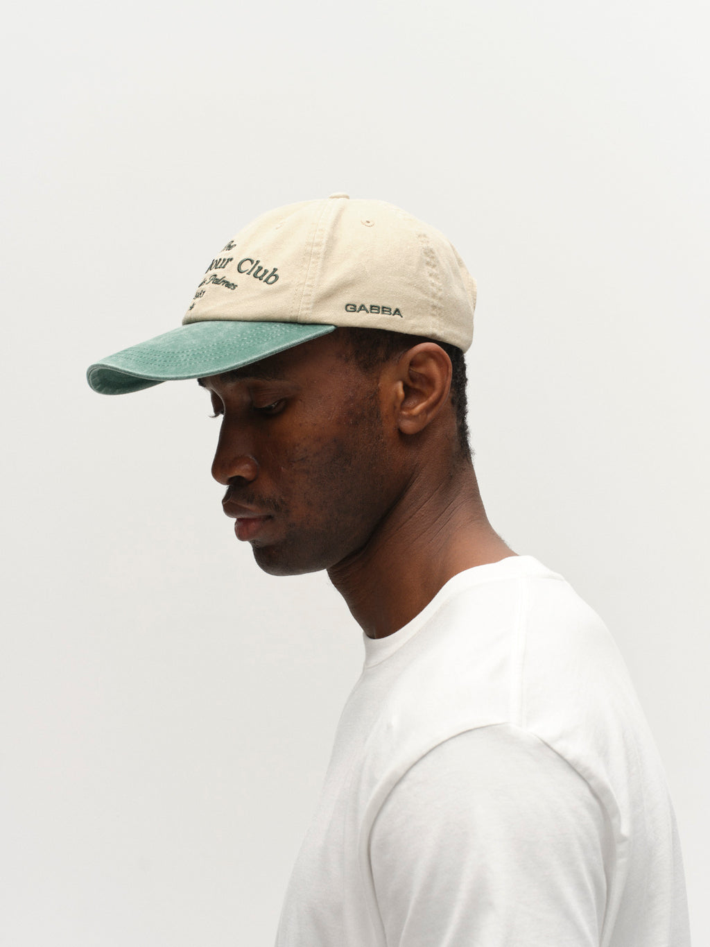 A man in profile, wearing the Gabba GABnbh Club Cap - Green and a plain white t-shirt, stands against a white background and looks downward.